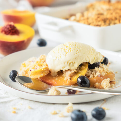 White plate with peach and blueberry crisp topped with white vanilla ice cream.