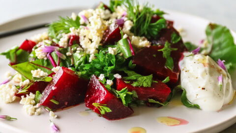 A plate with cubed beet salad, parsley and feta cheese on it.