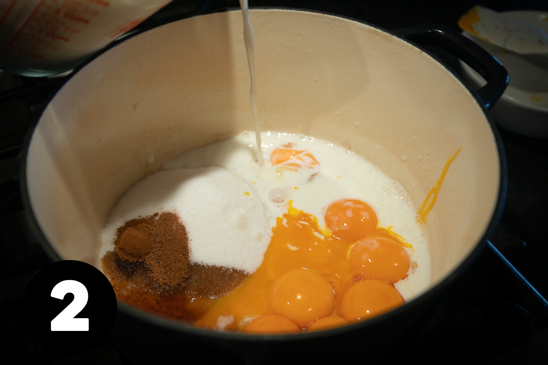 Milk being poured into the pot of egg yolks.