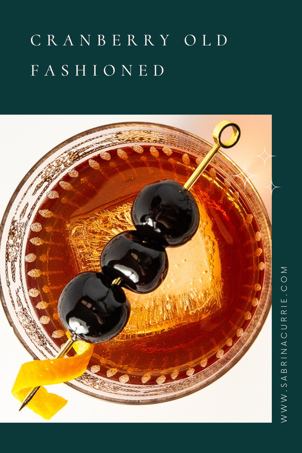 Looking into a glass with a dark, clear cocktail and an ice cube topped with a skewer of cherries and an orange twist.