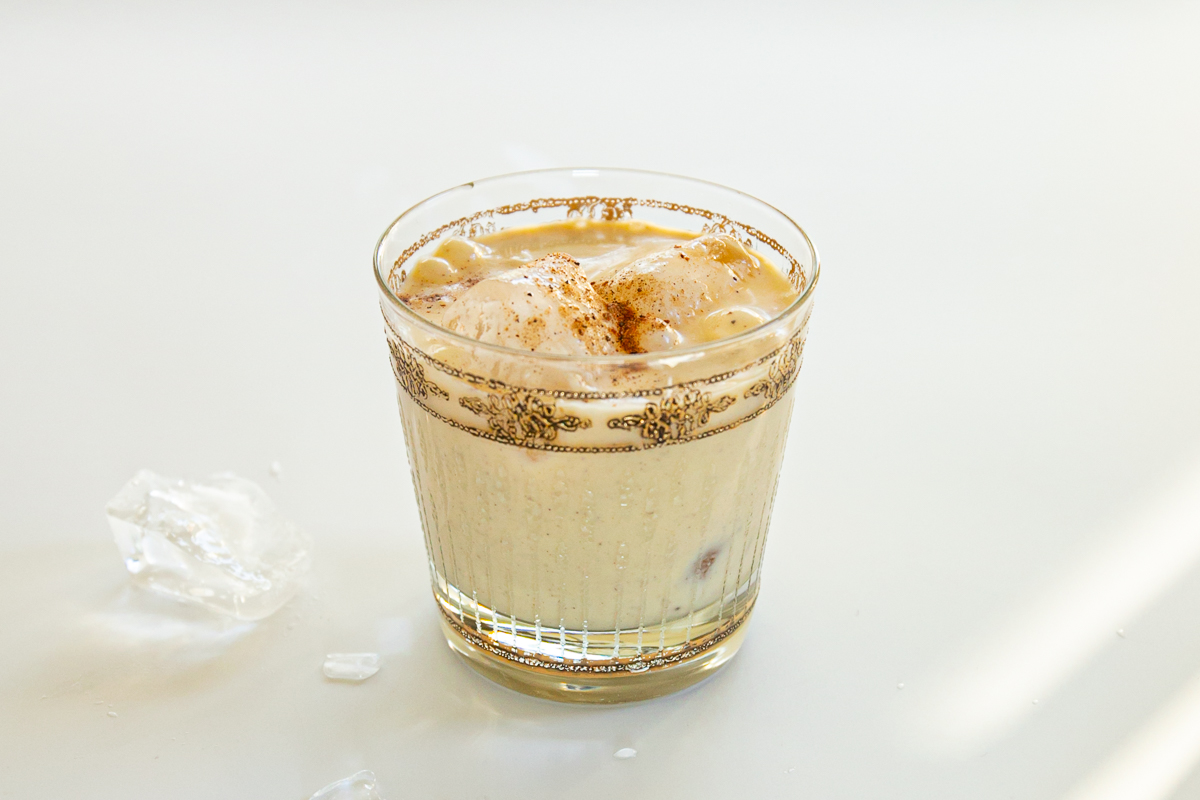 A glass of ice cubes and eggnog garnished with grated nutmeg on top.