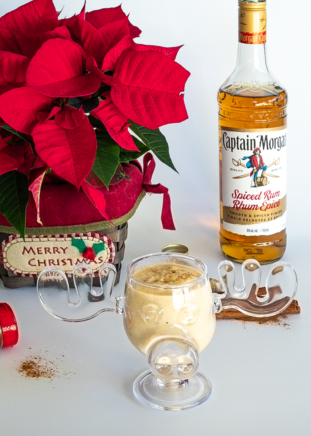 Eggnog in a moose mug with a poinsettia and a bottle of rum behind.