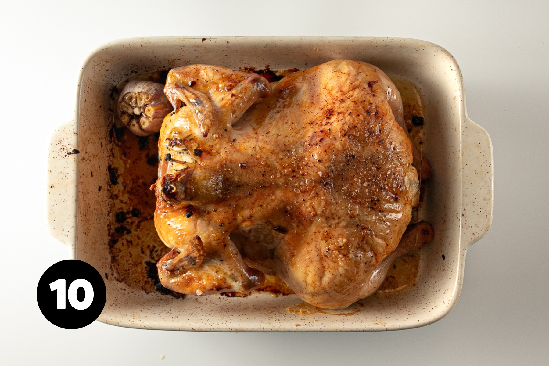 Dark golden and crisp whole roast chicken in a roasting pan.