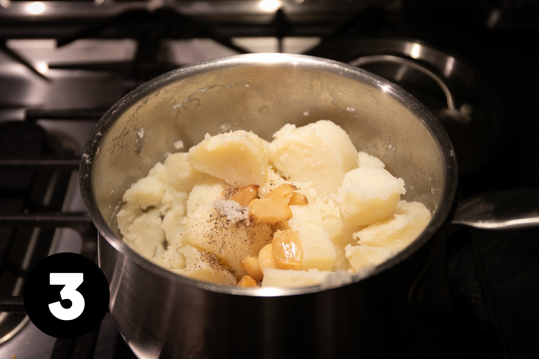 Cooked and drained potato pieces in a pot with cloves of garlic confit on top.