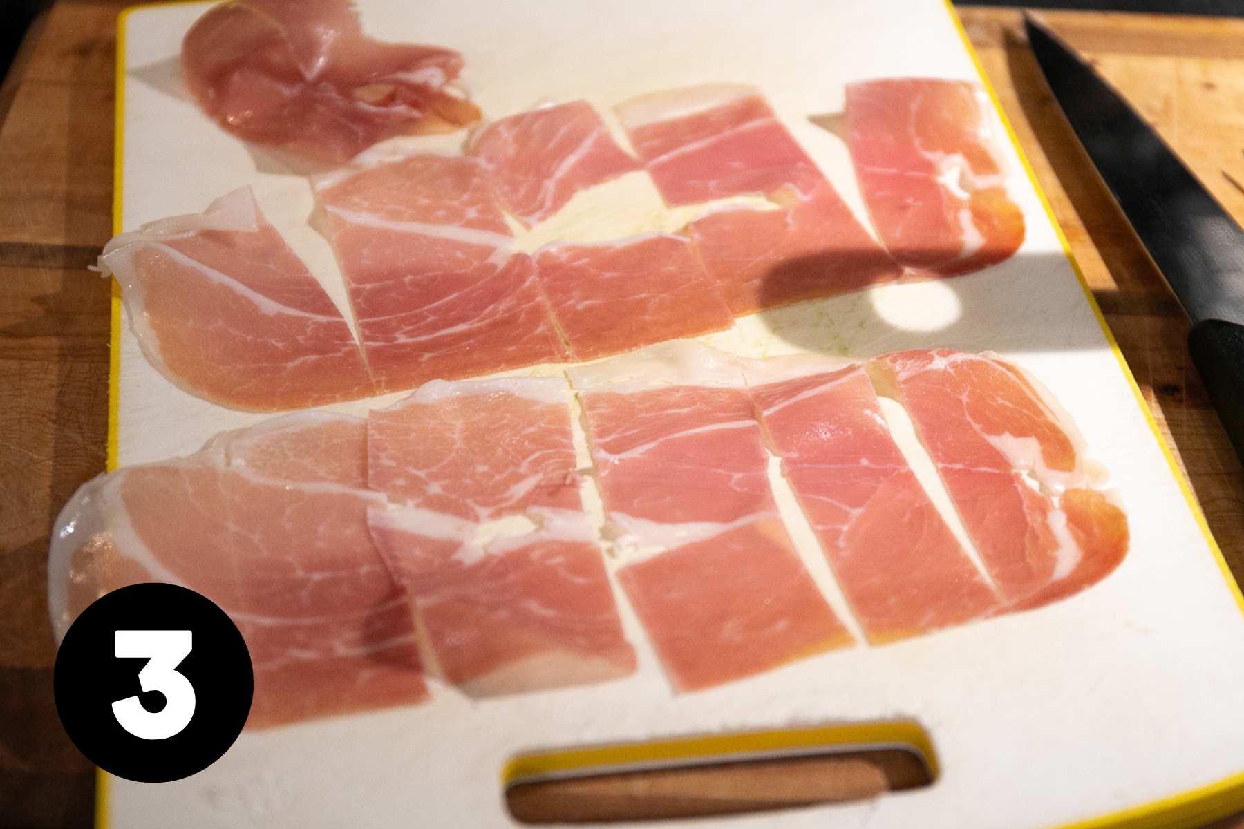 Prosciutto that's been sliced crosswise sitting on a cutting board.