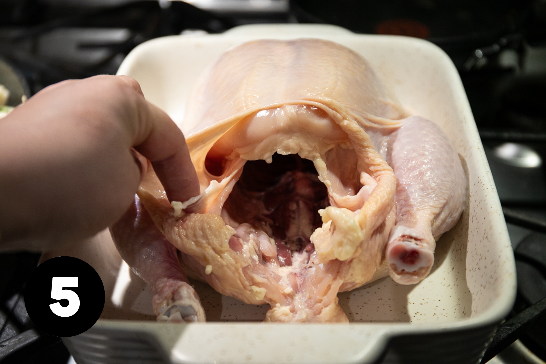 A whole raw chicken in a roasting pan.