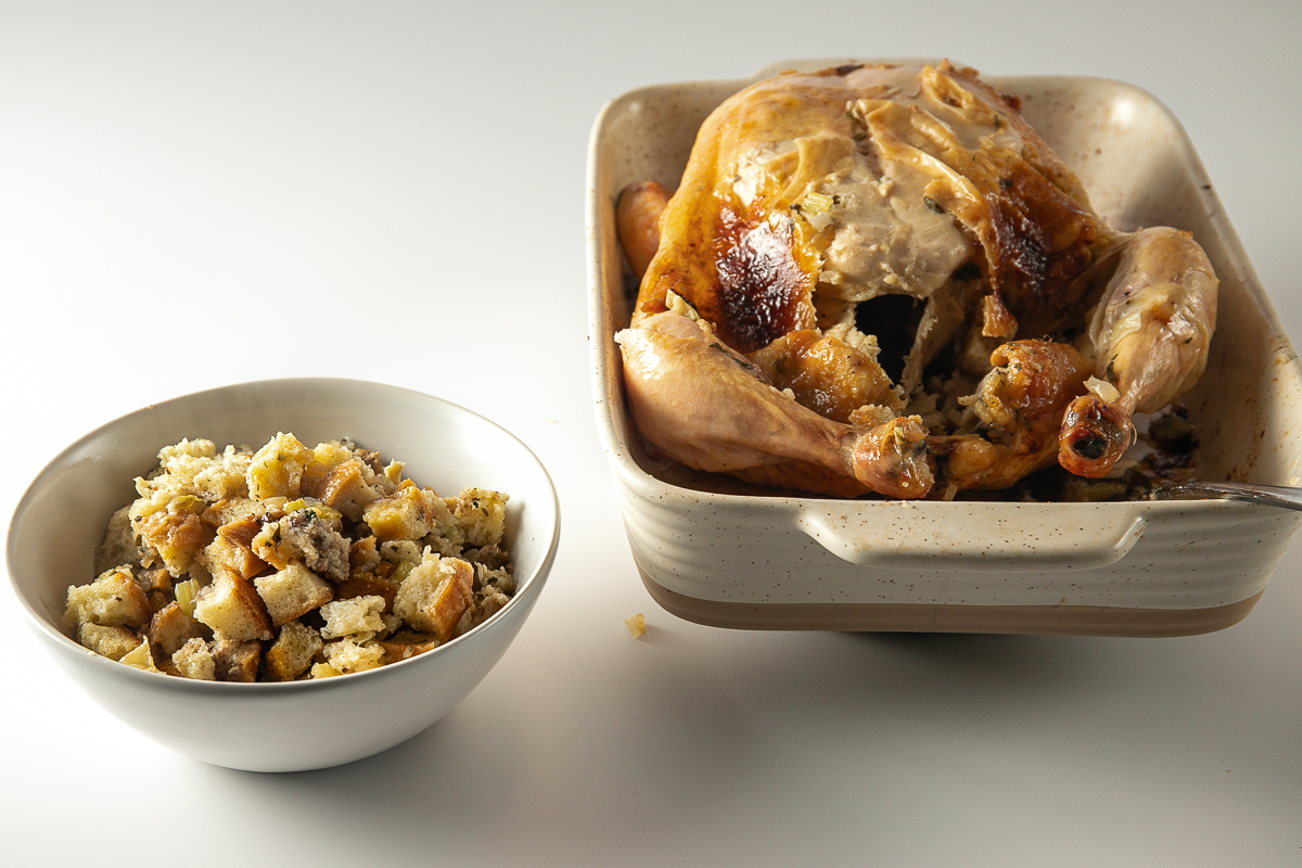 The cooked stuffing has been spooned into a bowl and is sitting beside the cooked chicken.