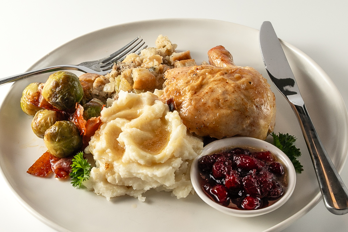 A plate of roast chicken, stuffing, mashed potatoes with gravy, brussels sprouts and cranberry sauce.