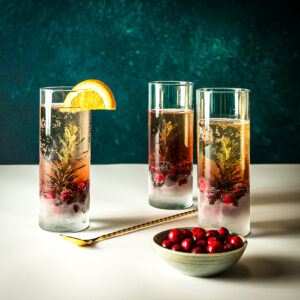 3 tall glasses filled with cranberry juice on the bottom and sparkling wine on tops with frozen sprigs of rosemary in the bottom half of the glasses.