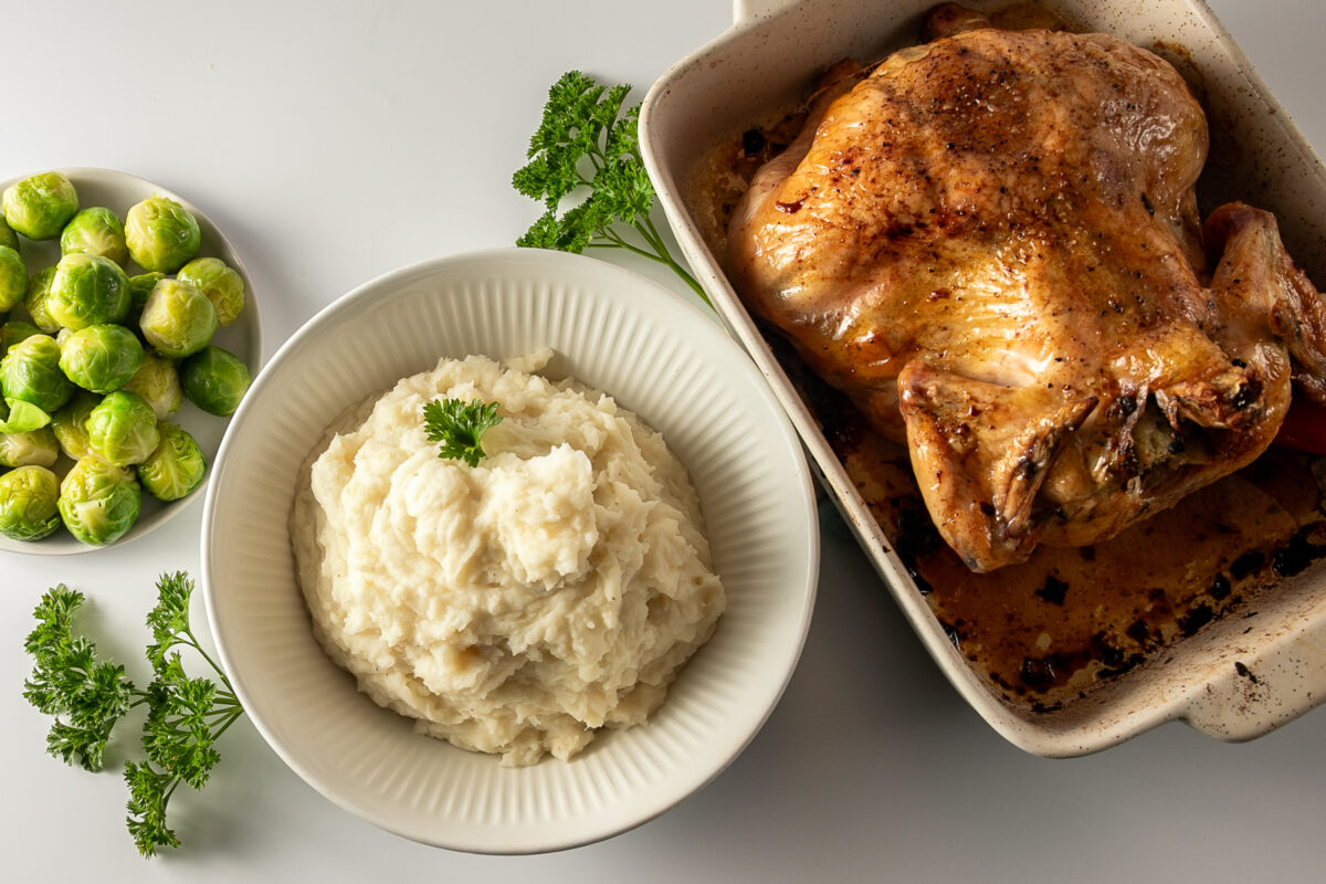 A roast chicken, a bowl of mashed potatoes, a bowl of Brussels sprouts and a few sprigs of parsley around.