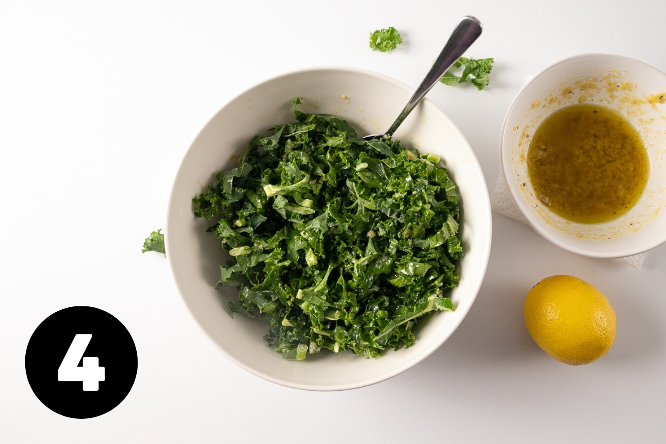 Bowl of dressed kale with the extra salad dressing and a lemon beside it.