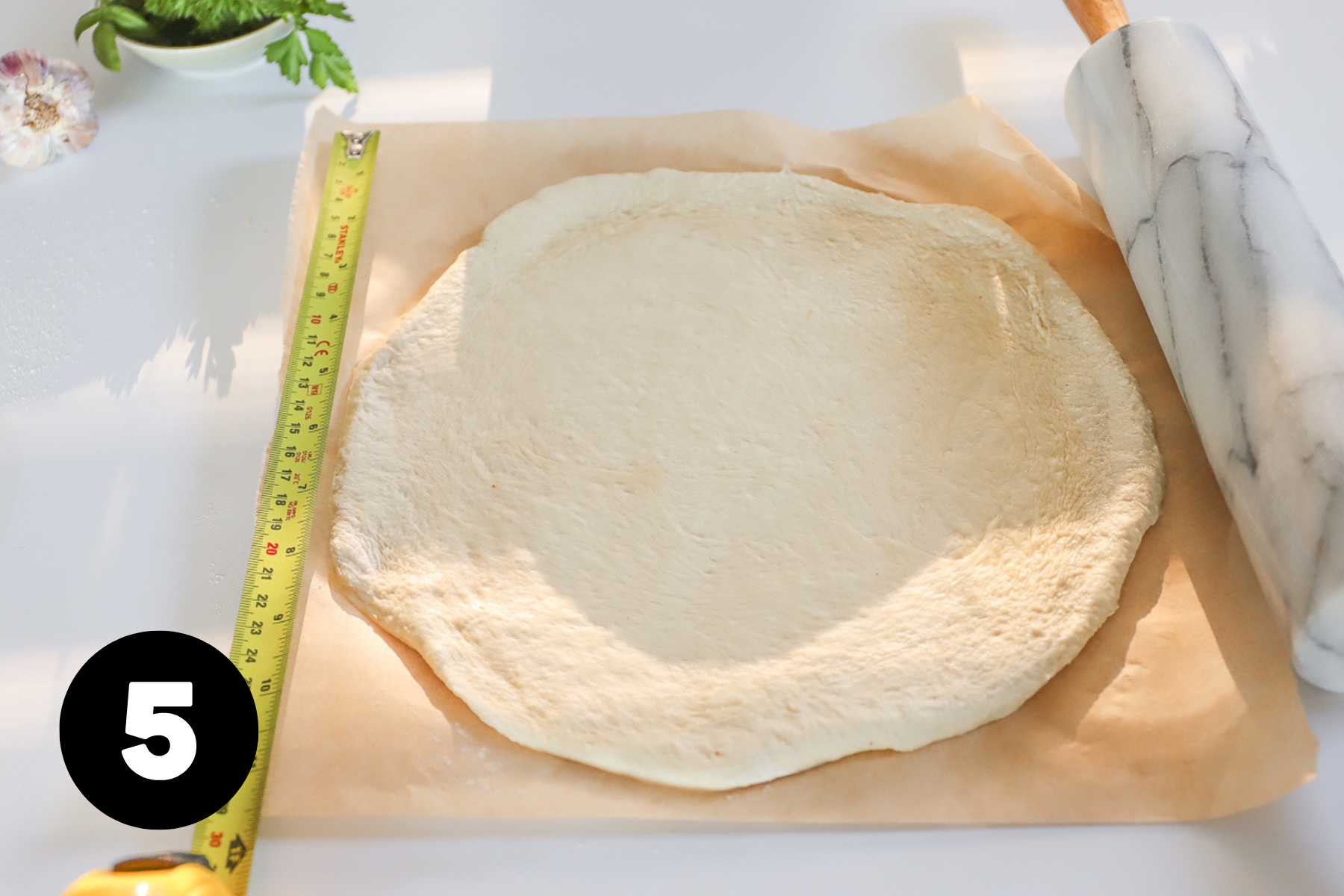 Pizza dough rolled out into a circle with a measuring tape alongside showing it is about 10 inches in diameter.