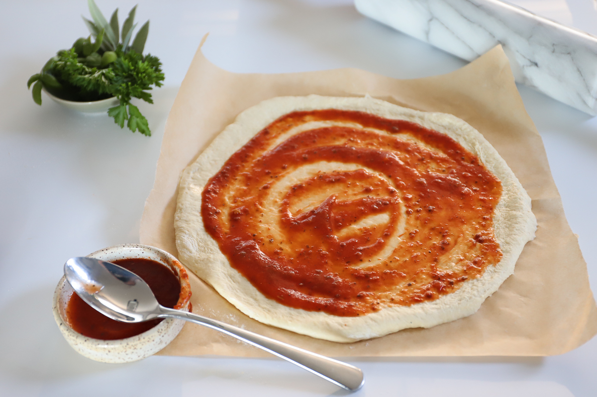A round of pizza dough topped with tomato sauce.