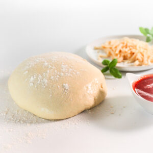 A ball of pizza dough dusted with flour, a plate of grated cheese and a bowl of tomato sauce.