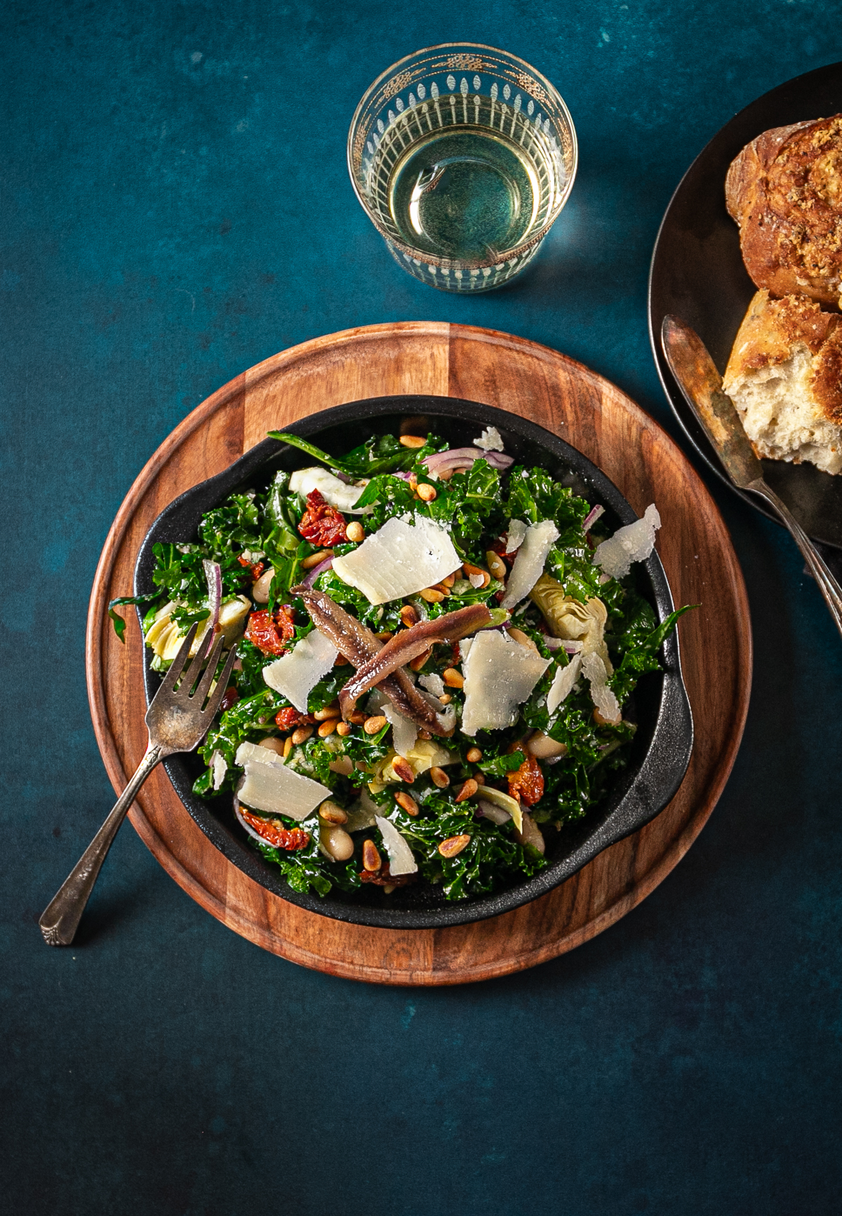 Bowl of salad topped with shards of parmesan cheese and anchovies.