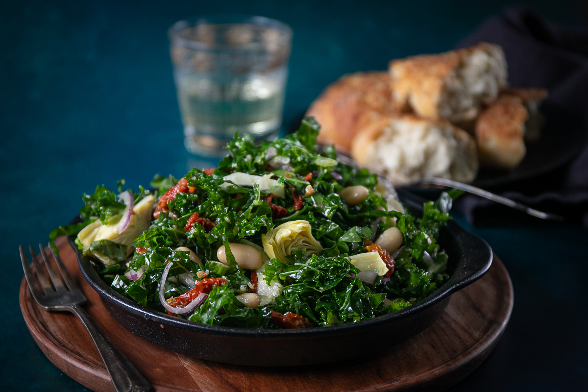 A bowl of colorful salad with a glass of water and some bread behind it.