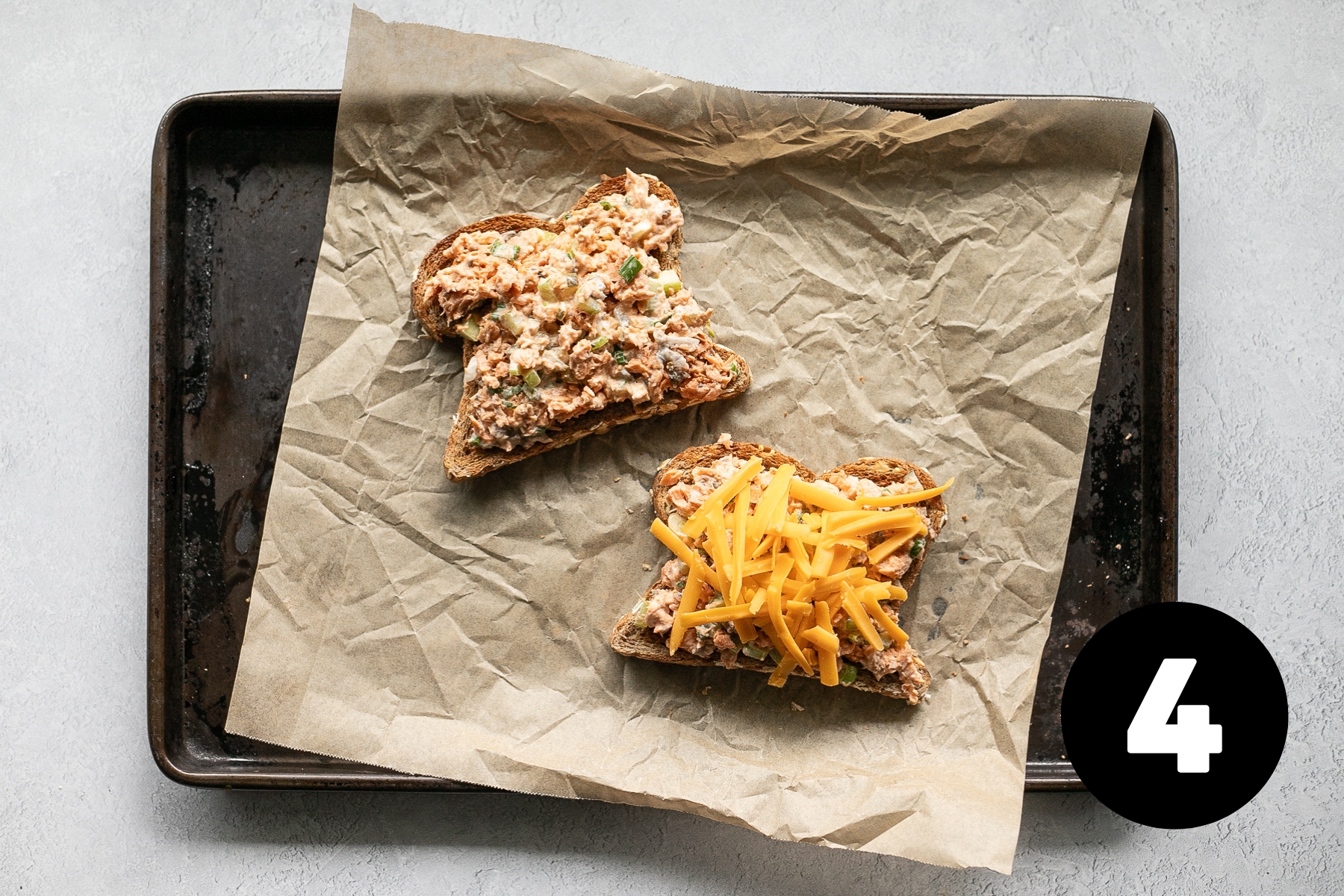 One slice of toast with salmon mixture spread over and the other has the salmon and a topping of shredded cheddar cheese.