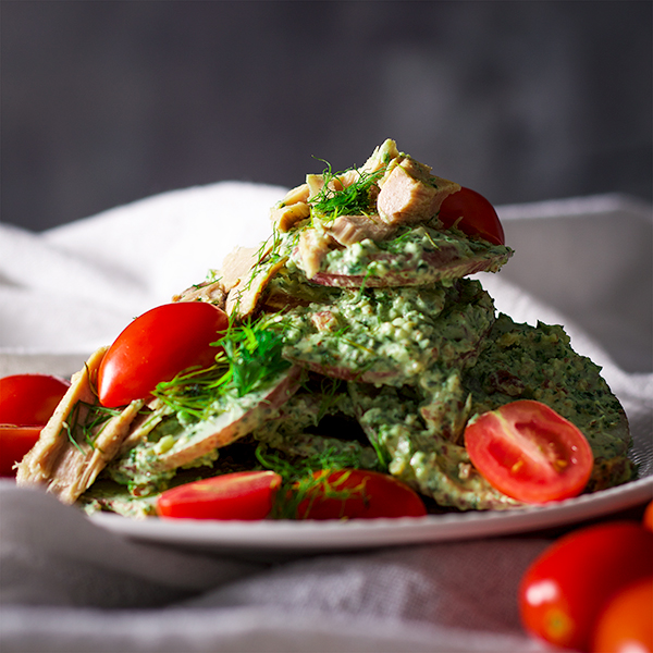 A pile of potatoes dressed with a thick green herb sauce and garnished with halved cherry tomatoes.