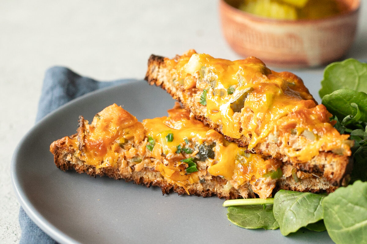 A closeup of the creamy, pickle and onion studded salmon mixture in the salmon melt that's been cut in half to show the inside.