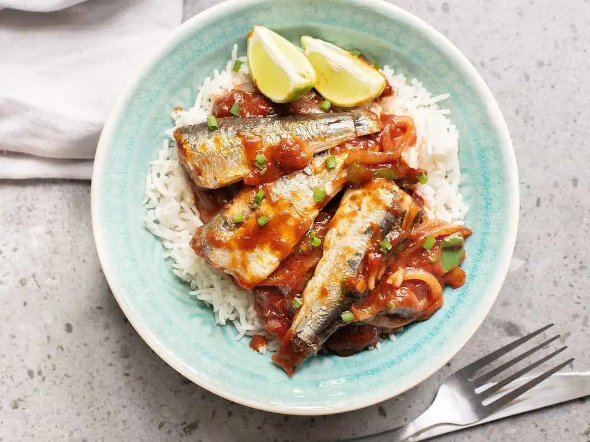 Tomato sauced sardine fillets on rice with a few wedges of lime beside.