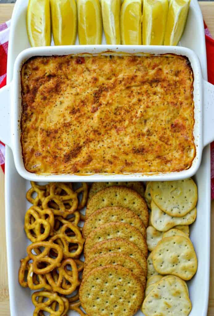 A casserole of tuna dip surrounded by lemon wedges and a variety of crackers.
