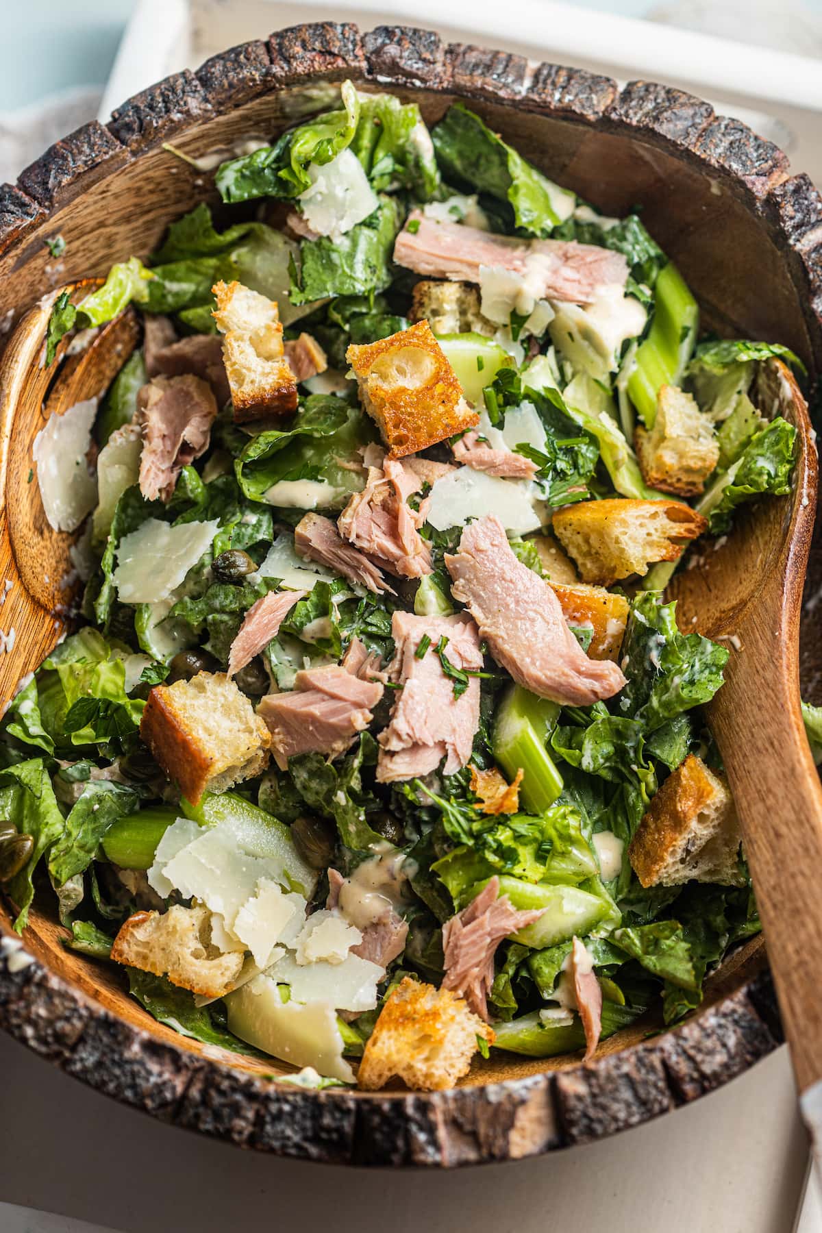 A wooden bowl of Caesar salad with croutons, tuna and grated parmesan cheese scattered around.