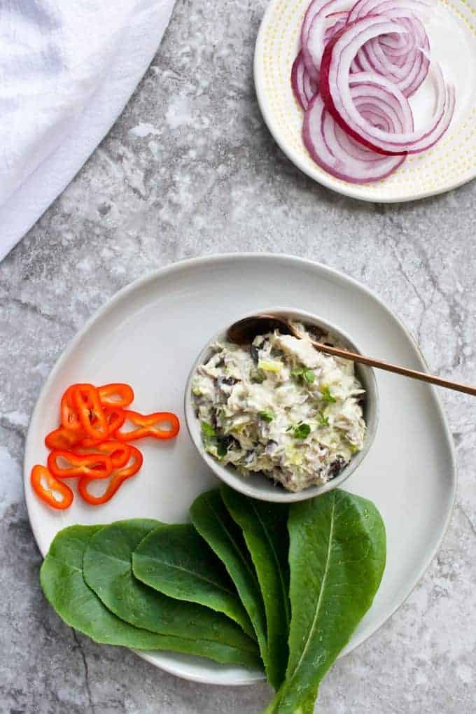 A bowl of creamy mackerel salad beside some salad greens and sliced red onion.