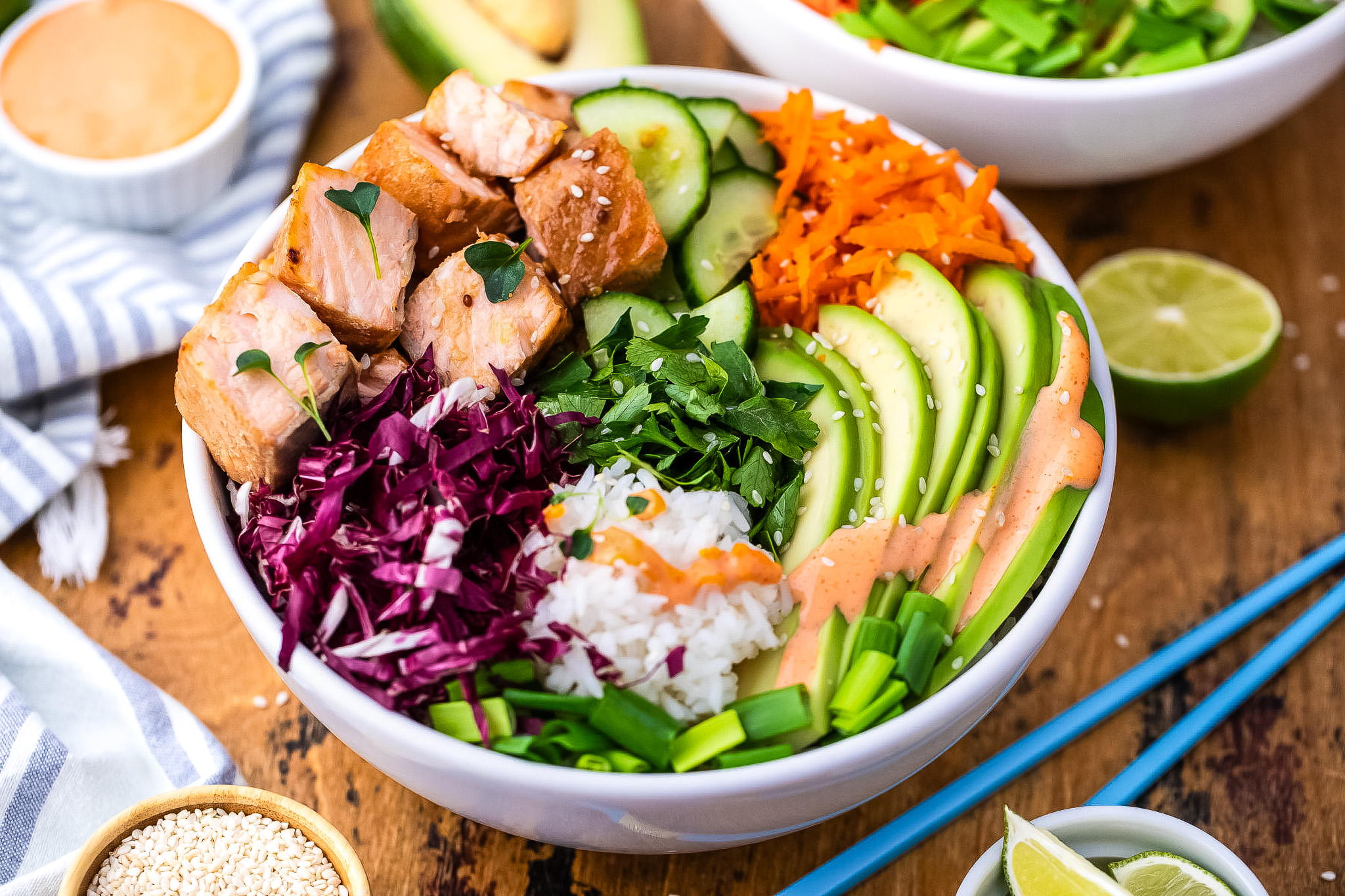 A poke bowl with cubes of cooked salmon, sliced and shredded vegetables, rice and topped with a spicy mayo sauce.