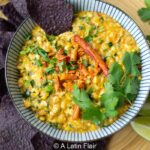 Bowl of corn dip studded with poblano peppers and topped with a sprig of cilantro.