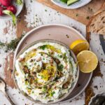 Bowls of cucumbers, radishes and creamy dip with sliced lemons and scattered spices around.