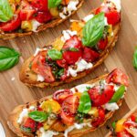 A platter of tomato and burrata topped crostini with basil leaves sprinkled over.