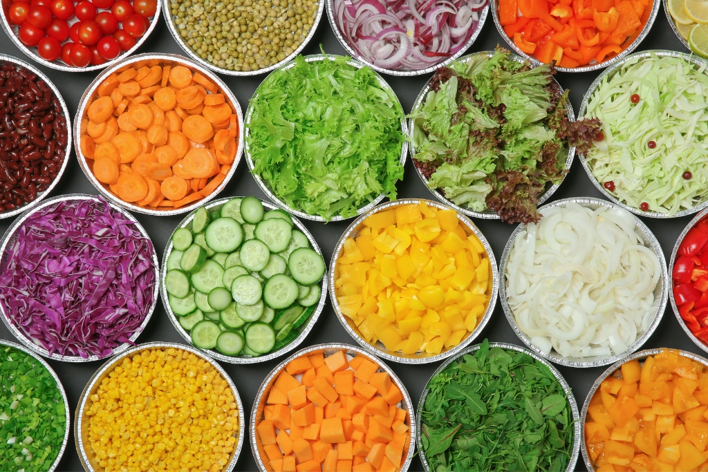 Rows of bowls, each filled with one sliced or diced salad ingredient.,