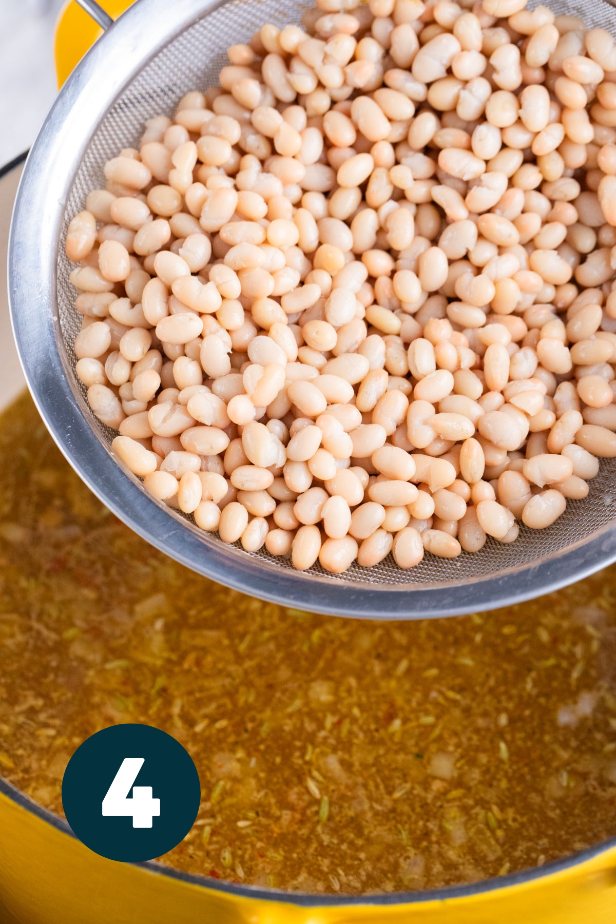 White cannellini beans being poured into the pot of soup.