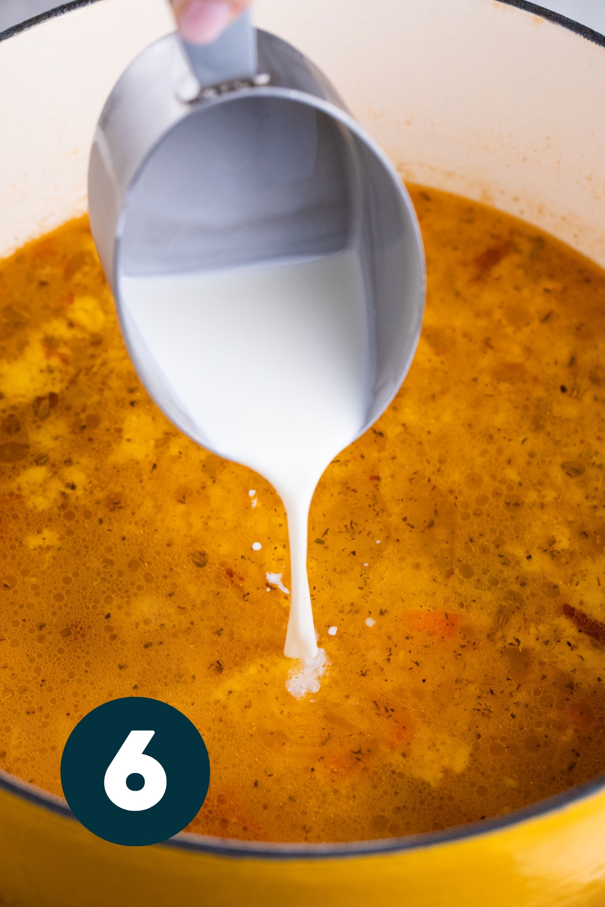 Cream being poured from a metal cup with spout into the soup.