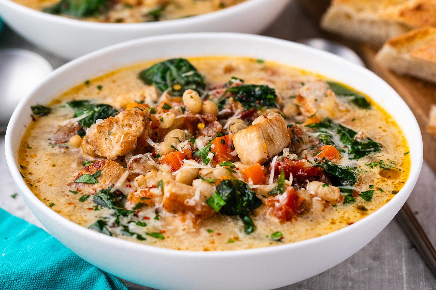 A bowl of chunky chicken soup with beans and spinach in it.