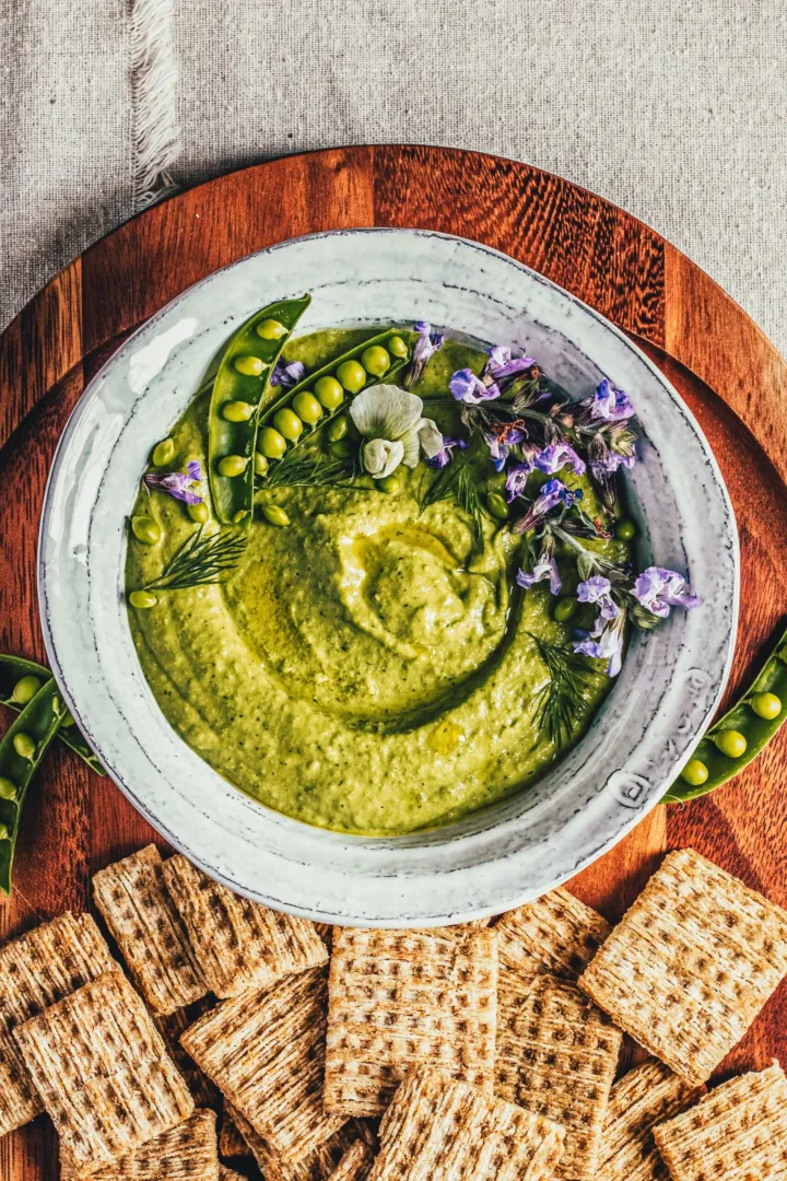 Creamy pea dip garnished with opened pea pods and tiny edible flowers.