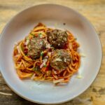 Three meatballs on top of spaghetti noodles and tomato sauce.