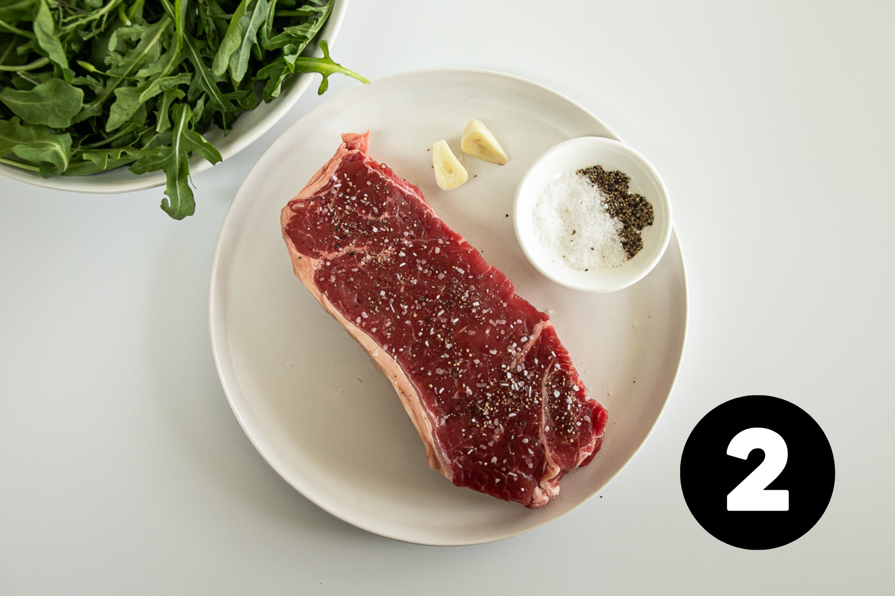 A raw steak topped with salt and pepper.
