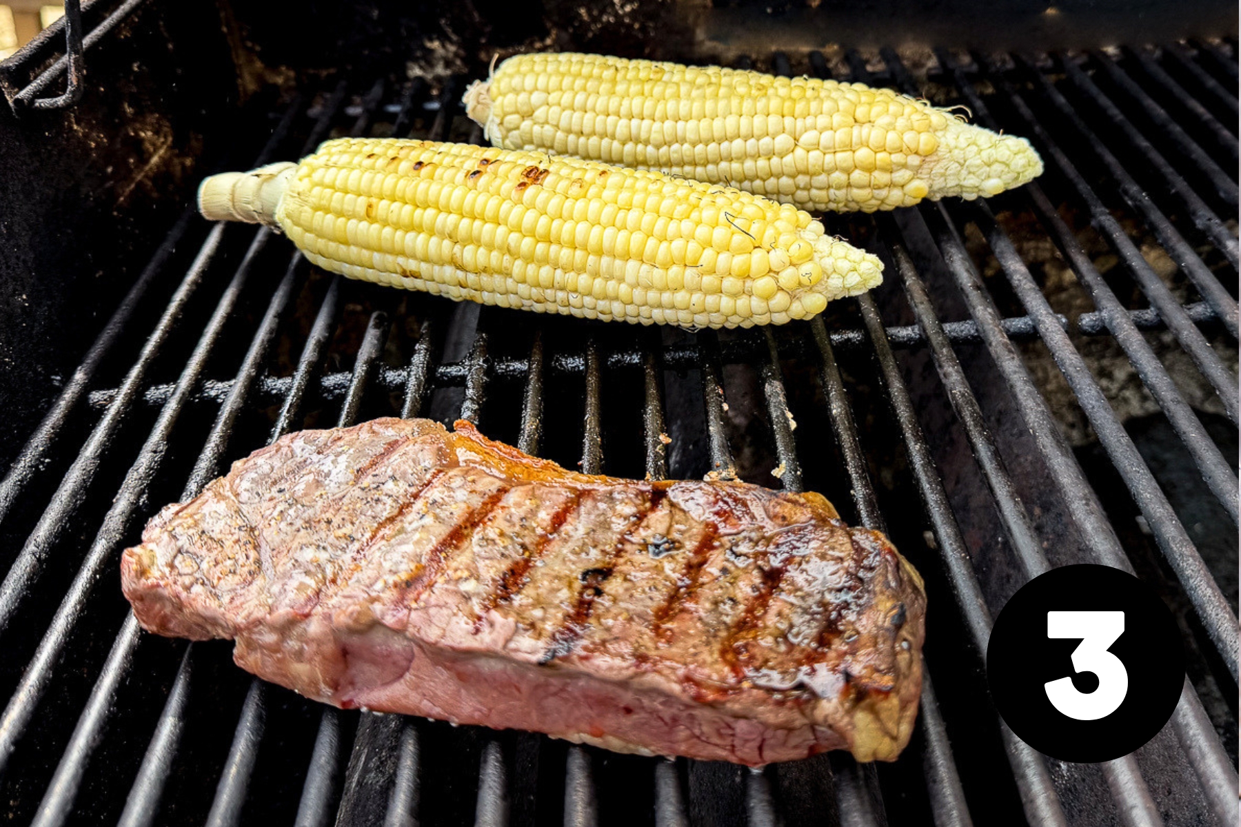 A steak and 2 cobs of corn on a barbecue grill.