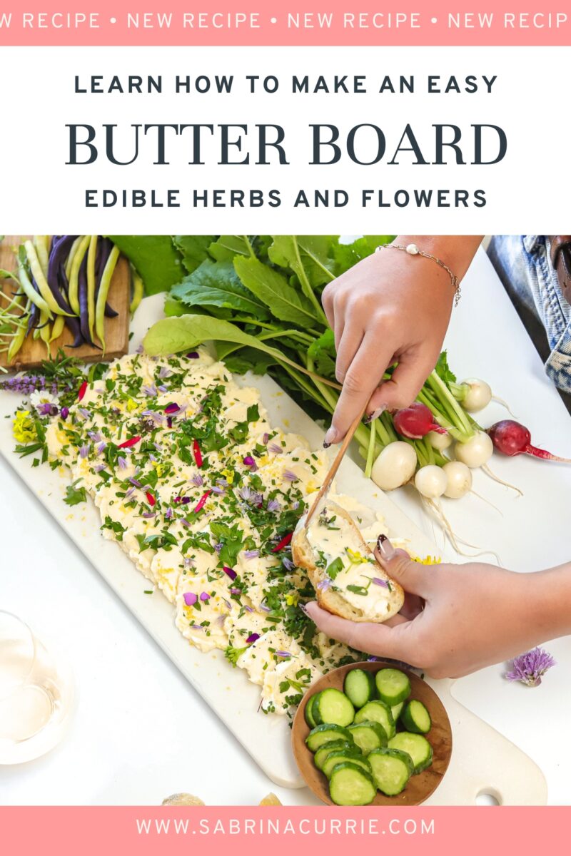 Hands spreading the herb flecked butter onto a piece of bread beside the herb and flower decorated butter board. The recipe title is on a banner above the photo.