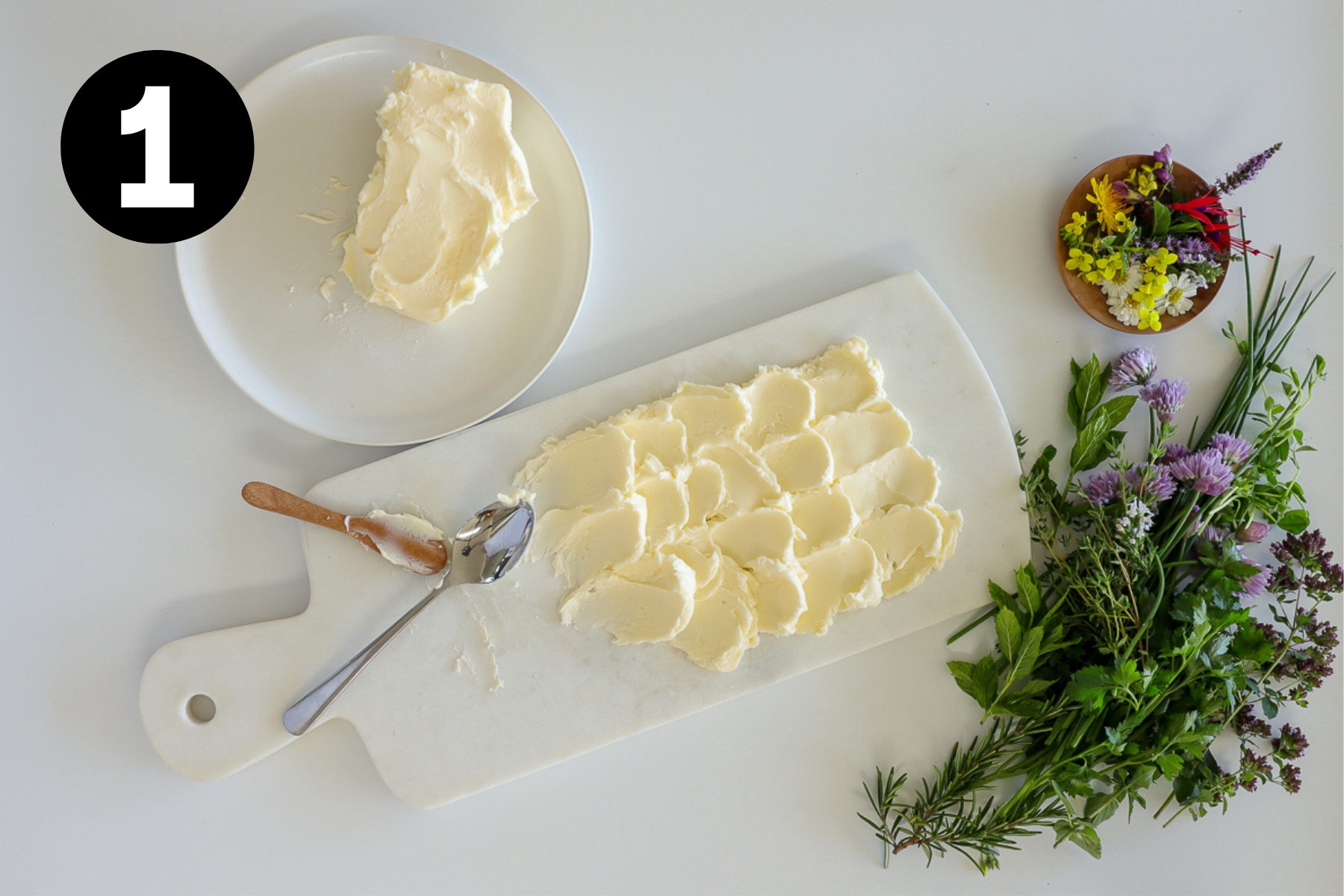 Butter spread in swirls over half of a marble serving board with herbs beside and a block of butter on the other side.