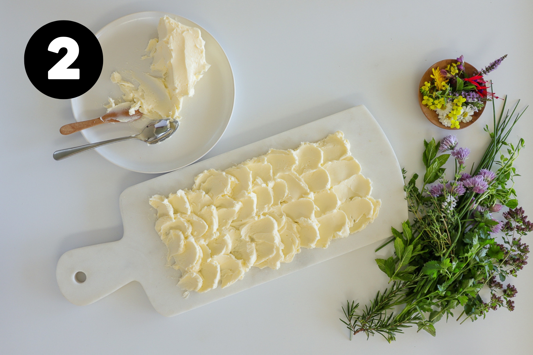 Butter spread in swirls over a marble serving board with herbs beside and a block of butter on the other side.
