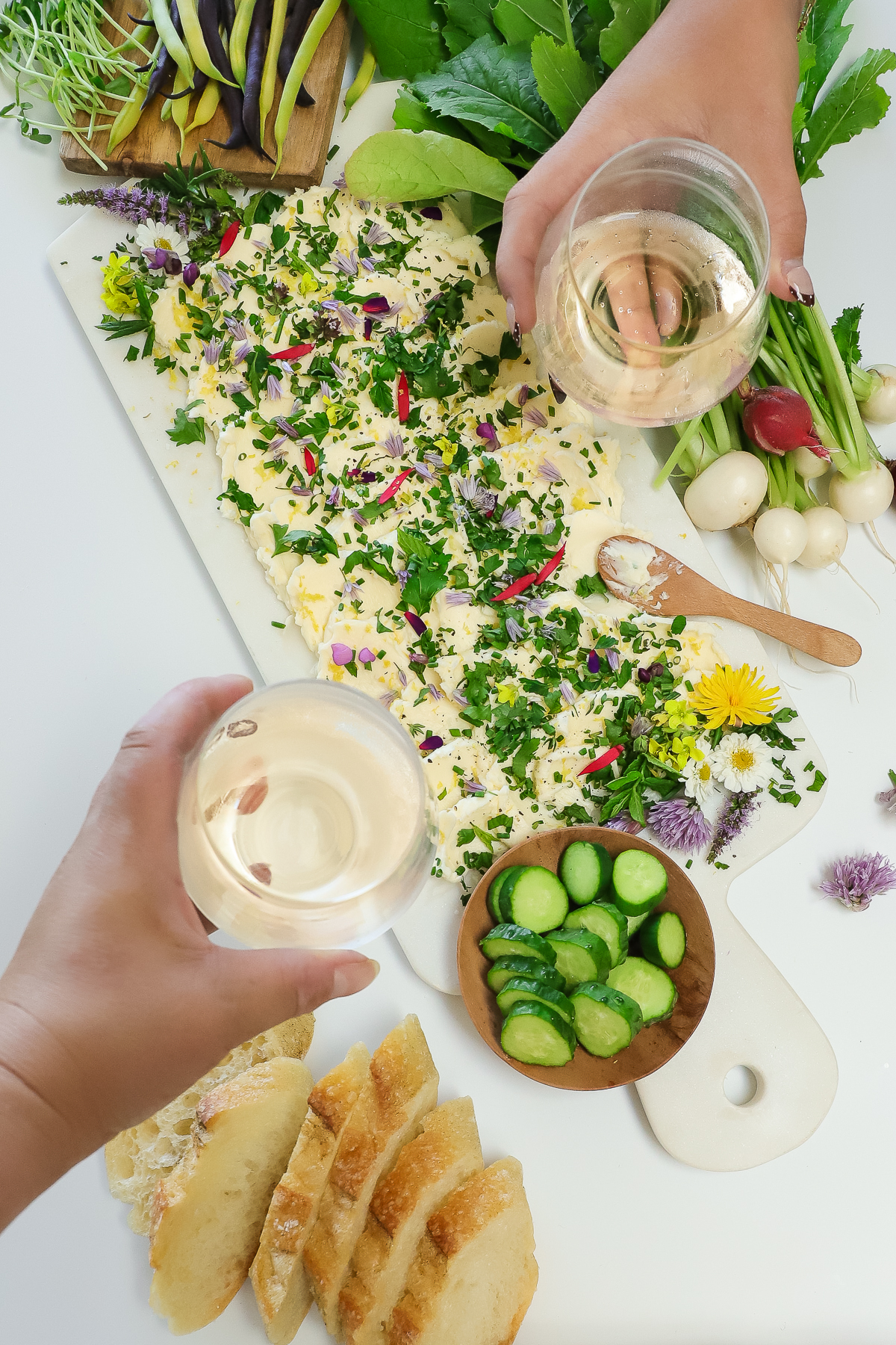 Two wine glasses held above the chive flower butter board to toast cheers.
