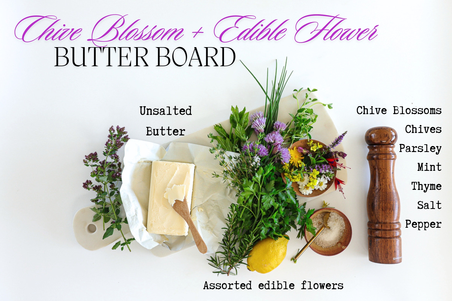 All the ingredients for the butter board recipe on a countertop. Shown is butter, a lemon, salt, pepper and a large bunch of assorted herbs and edible flowers.
