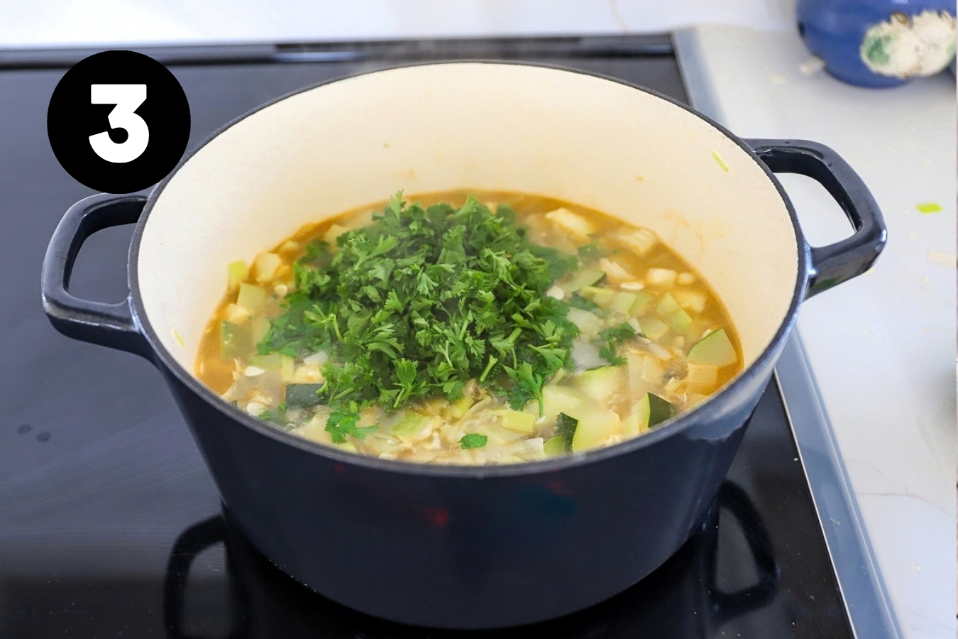 A cup of chopped parsley added onto the pot of soup.