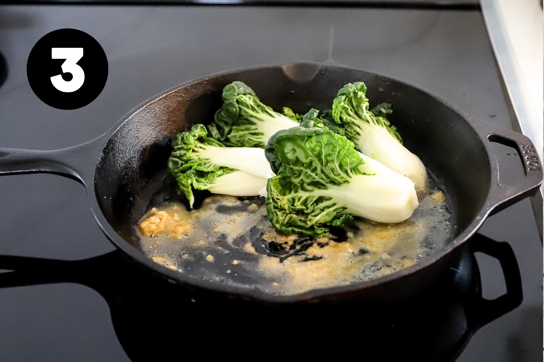 Fresh halved and whole baby bok choys being placed in the pan over foaming miso mixture.