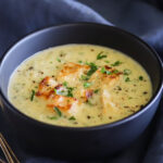 A bowl of parsley flecked creamy soup topped with toasted croutons on a dark blue linen tablecloth.