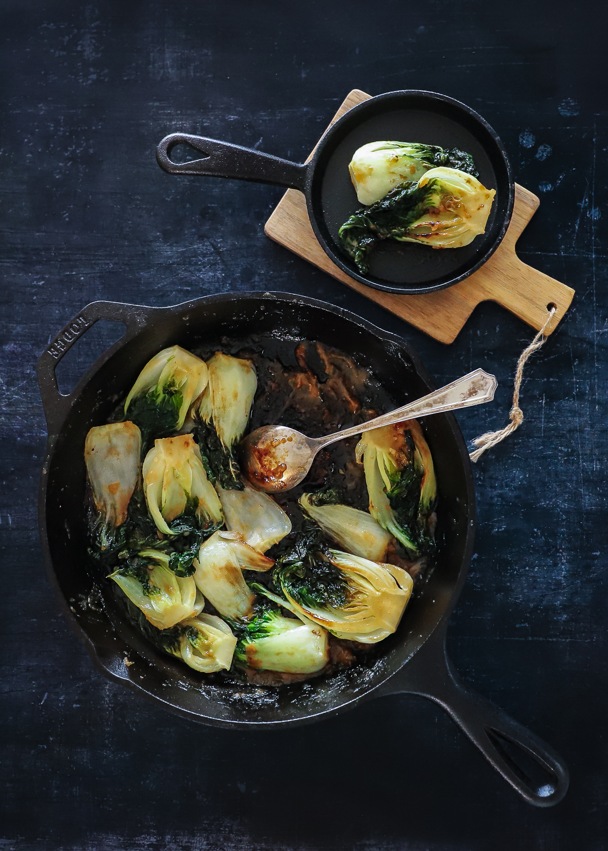 One large and one small cast iron frying pan with caramelized baby bok choy halves.