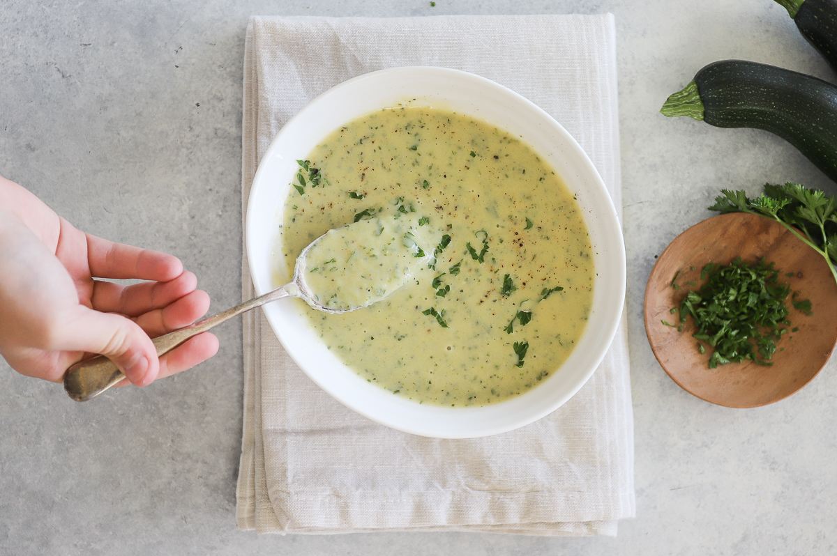 A hand scooping up a spoonful of soup from a bowl of soup set on a cloth napkin.