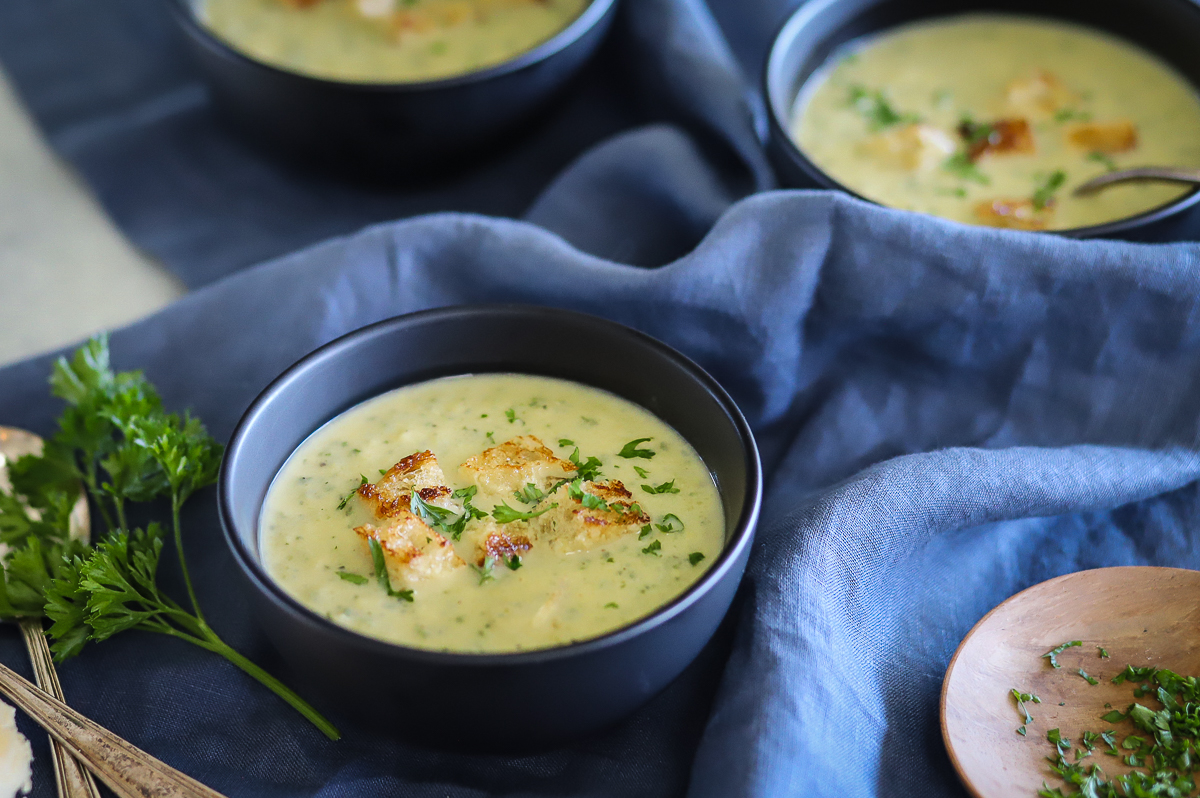 Bowl of soup with a side of chopped parsley on a small wooden plate.